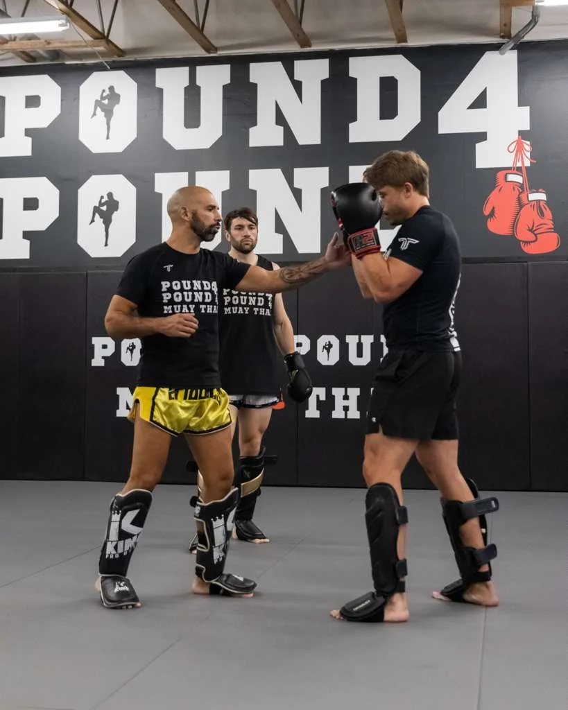 Pound 4 Pound coach demonstrating Muay Thai technique with a student while another member watches during class