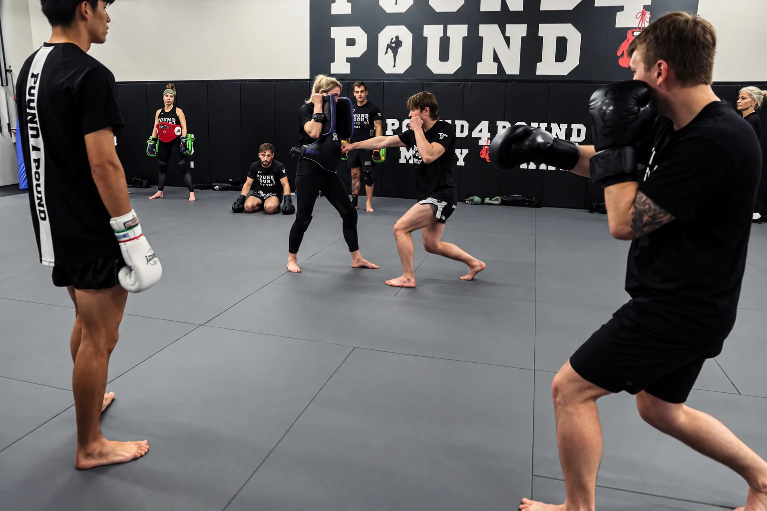 Pound 4 Pound Muay Thai students resting between rounds against the wall inside the Littleton training gym