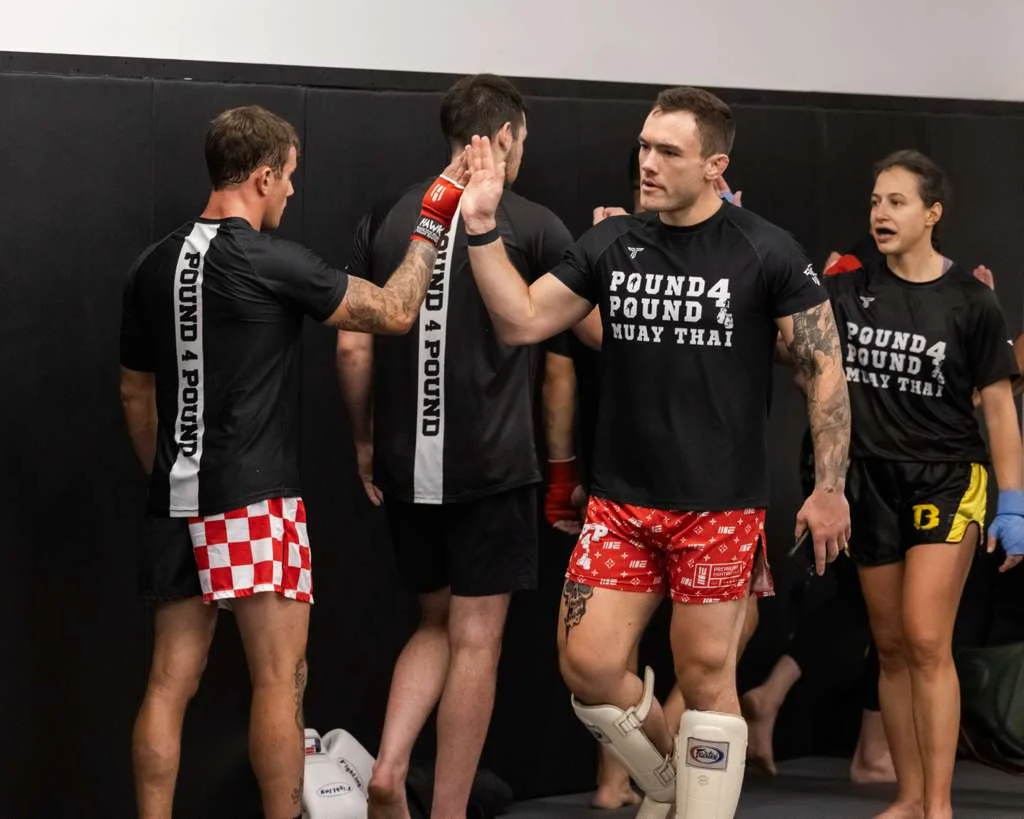 Pound 4 Pound Muay Thai students and coach sharing a high five after a training round in Littleton